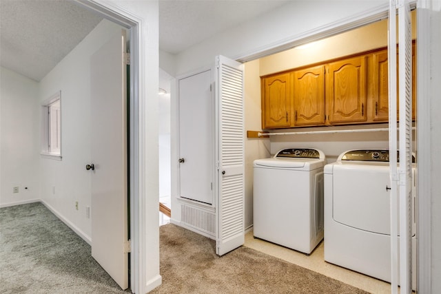 laundry room with baseboards, washing machine and dryer, light carpet, cabinet space, and a textured ceiling