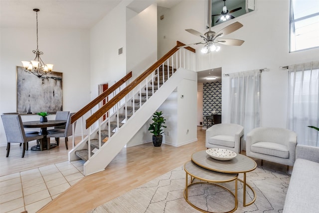 living area featuring visible vents, stairs, ceiling fan with notable chandelier, a towering ceiling, and wood finished floors