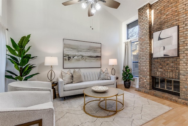 living room featuring a ceiling fan, a brick fireplace, wood finished floors, and a high ceiling