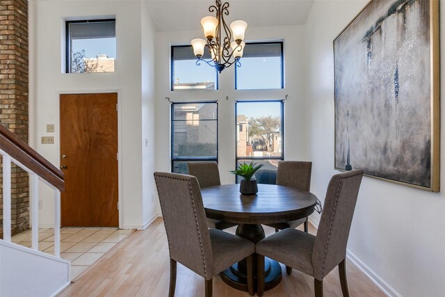 dining space featuring stairs, light wood-type flooring, a towering ceiling, and a chandelier