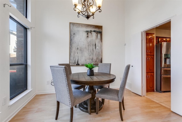 dining area featuring light wood finished floors, a chandelier, baseboards, and a towering ceiling