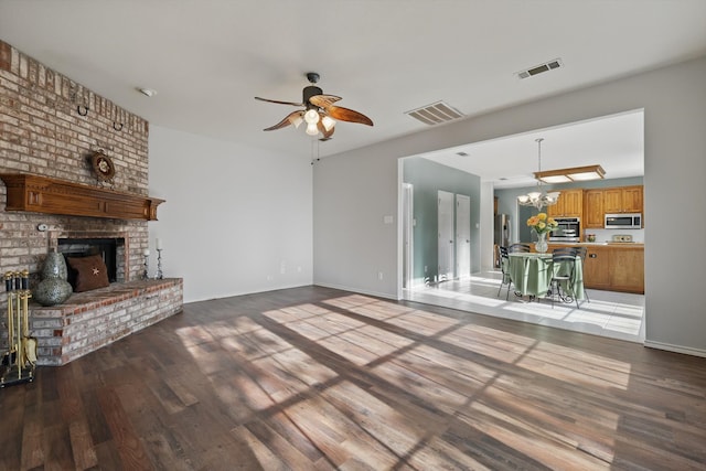 unfurnished living room with visible vents, ceiling fan with notable chandelier, a fireplace, and light wood-style floors