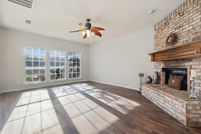 unfurnished living room with a brick fireplace, dark wood-style floors, and visible vents