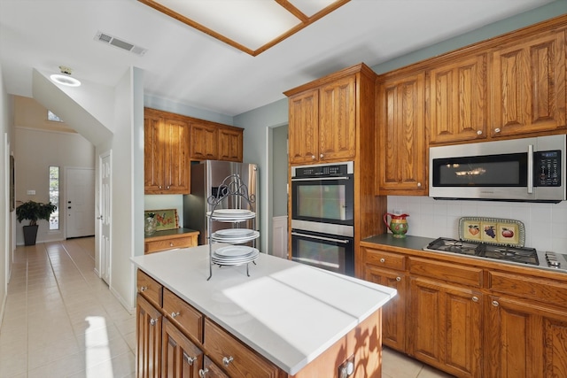 kitchen with light tile patterned floors, brown cabinetry, visible vents, stainless steel appliances, and decorative backsplash