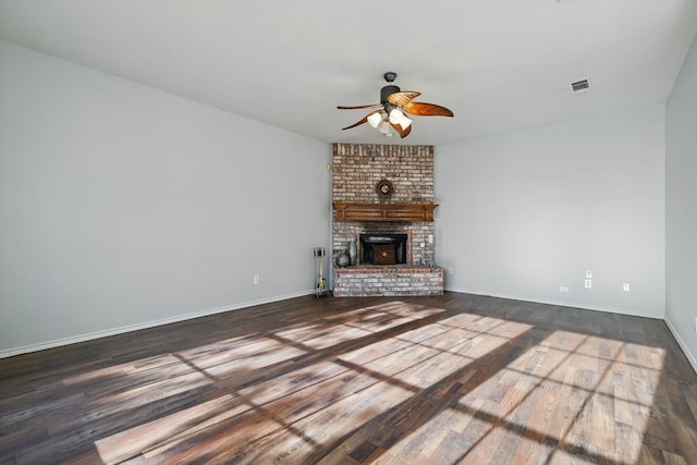 unfurnished living room with visible vents, wood finished floors, baseboards, a brick fireplace, and ceiling fan