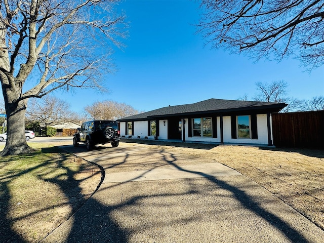 view of front of property featuring roof with shingles, driveway, and fence