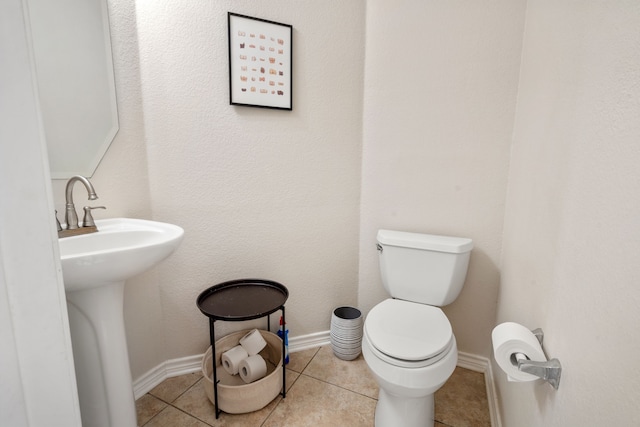 half bathroom with tile patterned flooring, toilet, baseboards, and a sink