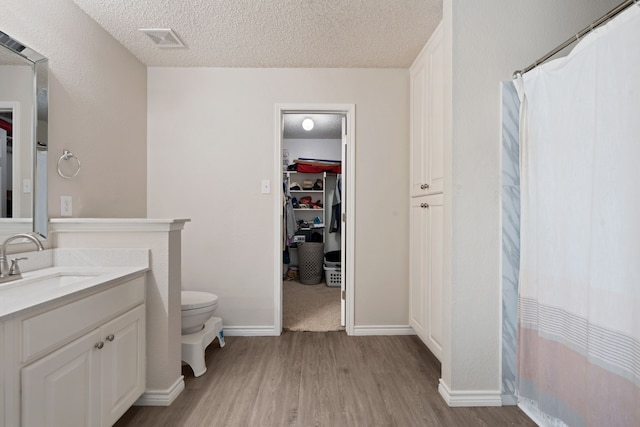 full bath featuring visible vents, toilet, vanity, wood finished floors, and a textured ceiling