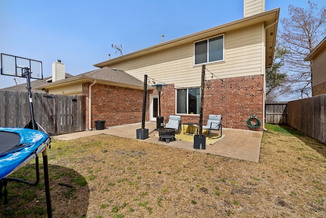 back of property with brick siding, a patio, a chimney, and a trampoline