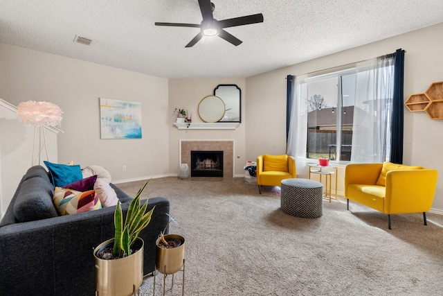 living room featuring visible vents, a tiled fireplace, a textured ceiling, carpet flooring, and baseboards