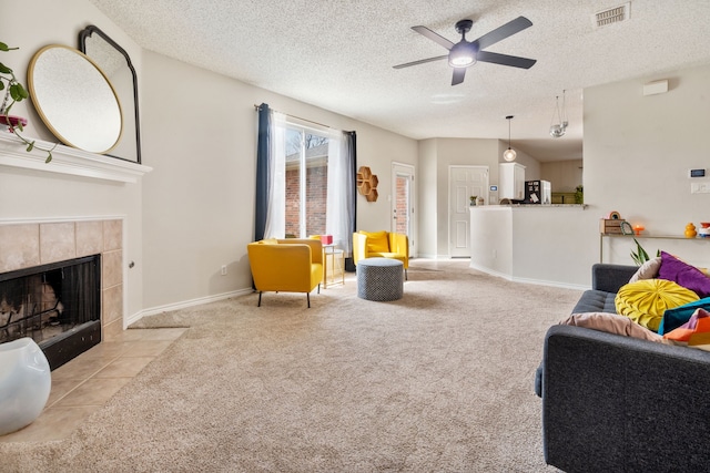 living area with a ceiling fan, visible vents, a tile fireplace, a textured ceiling, and carpet flooring