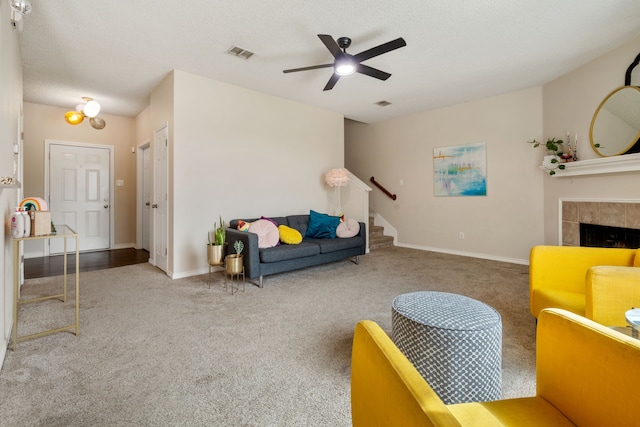 carpeted living area featuring stairway, a ceiling fan, visible vents, a textured ceiling, and a tiled fireplace