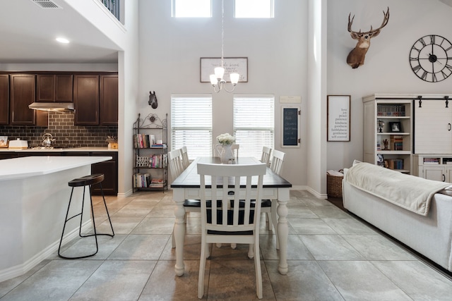 dining area with light tile patterned floors, visible vents, baseboards, a towering ceiling, and a chandelier