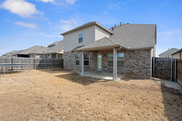 rear view of house featuring a patio, a trampoline, a fenced backyard, roof with shingles, and brick siding