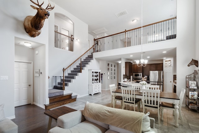 living area with visible vents, a notable chandelier, a high ceiling, baseboards, and stairs