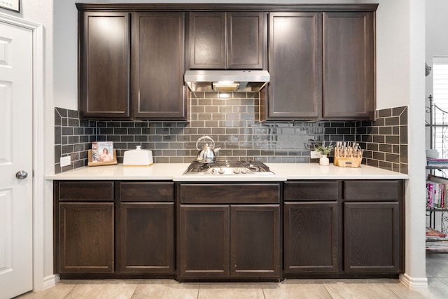 kitchen featuring under cabinet range hood, dark brown cabinetry, light countertops, and stainless steel gas cooktop