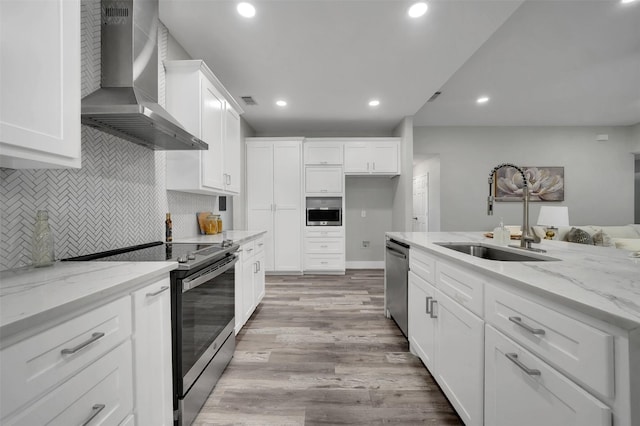 kitchen featuring wall chimney range hood, a sink, decorative backsplash, light wood-style floors, and stainless steel appliances