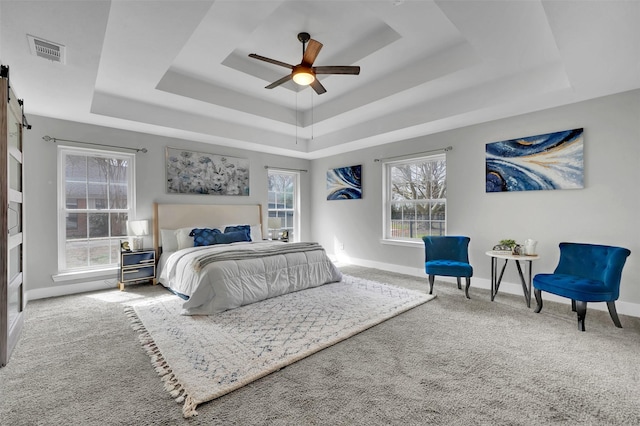 carpeted bedroom with visible vents, baseboards, a tray ceiling, and a barn door