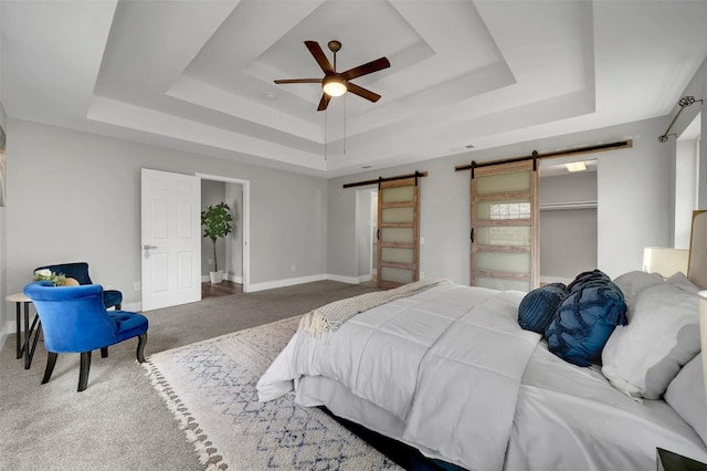 carpeted bedroom with baseboards, a ceiling fan, a tray ceiling, and a barn door