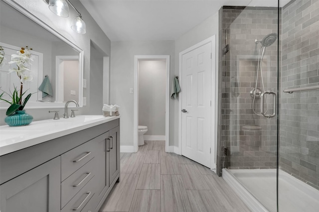 bathroom with double vanity, toilet, a sink, baseboards, and a stall shower