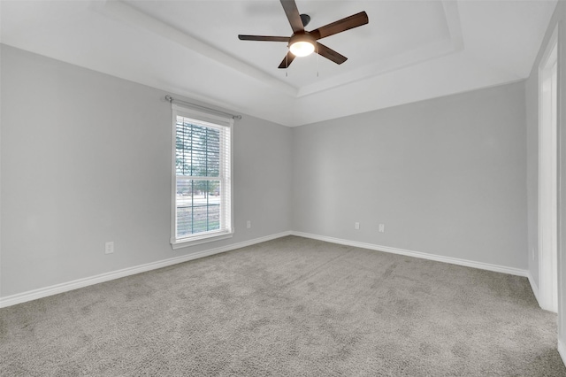 carpeted empty room featuring ceiling fan, baseboards, and a raised ceiling