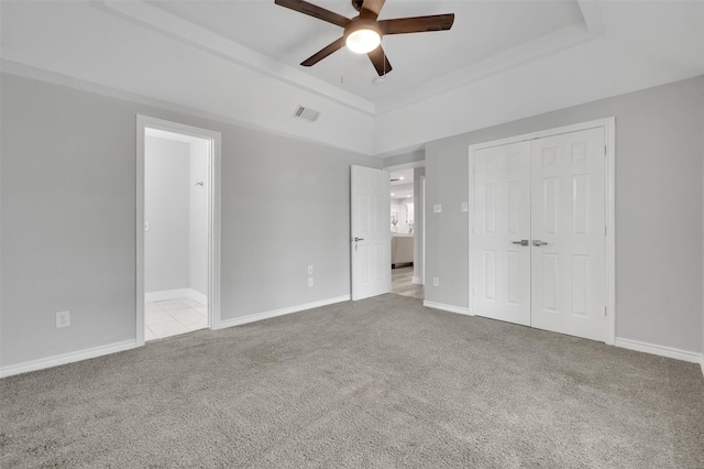 unfurnished bedroom with a raised ceiling, visible vents, a closet, carpet flooring, and ceiling fan