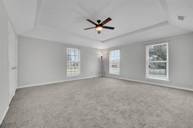 empty room featuring a tray ceiling, visible vents, a wealth of natural light, and ceiling fan