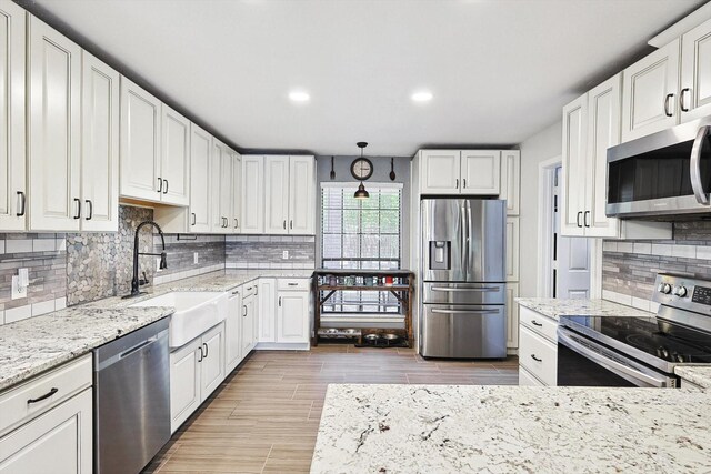 kitchen with backsplash, light stone countertops, appliances with stainless steel finishes, white cabinets, and a sink