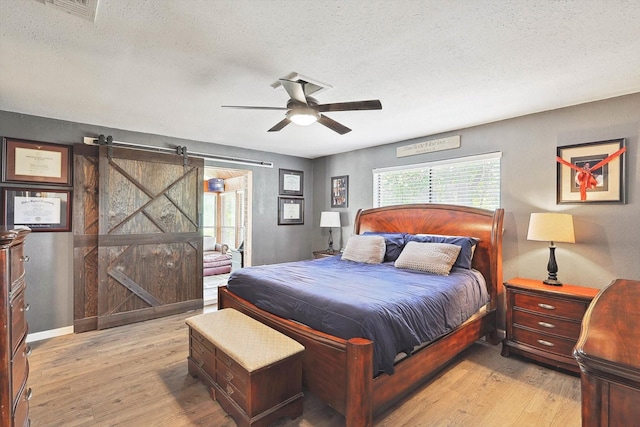 bedroom featuring a barn door, visible vents, a textured ceiling, and light wood-style floors