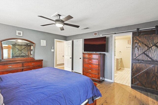 bedroom featuring a ceiling fan, visible vents, hardwood / wood-style flooring, a barn door, and connected bathroom