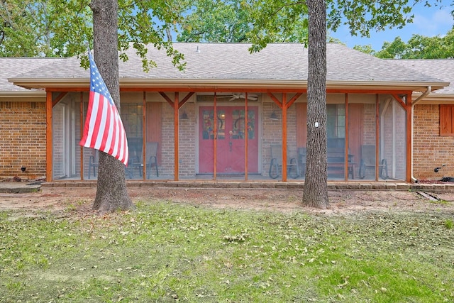 view of front of home with a front yard, brick siding, a sunroom, and a shingled roof