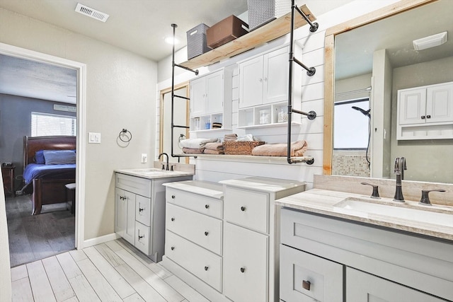 ensuite bathroom featuring ensuite bath, wood finished floors, visible vents, and a sink