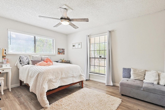 bedroom featuring baseboards, multiple windows, a textured ceiling, and light wood finished floors