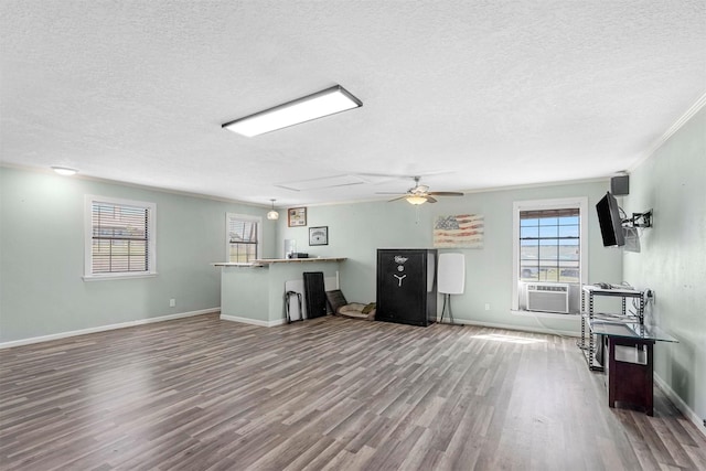 unfurnished living room with cooling unit, baseboards, a textured ceiling, and wood finished floors