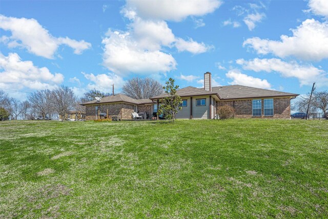 rear view of property with a lawn, brick siding, and a chimney