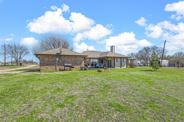 back of property featuring a yard, brick siding, a chimney, and fence