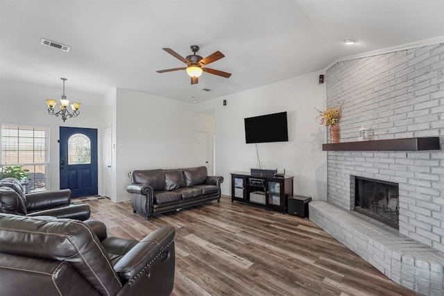 living area featuring visible vents, a brick fireplace, lofted ceiling, ceiling fan with notable chandelier, and wood finished floors