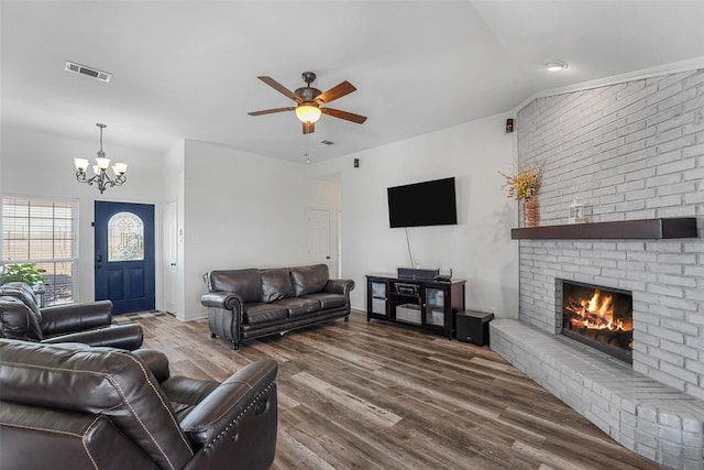 living area with visible vents, ceiling fan with notable chandelier, wood finished floors, a fireplace, and lofted ceiling