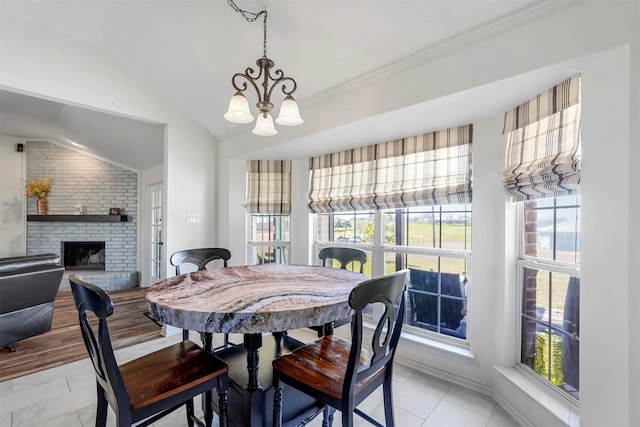 dining room with vaulted ceiling, a brick fireplace, a notable chandelier, and light wood-type flooring