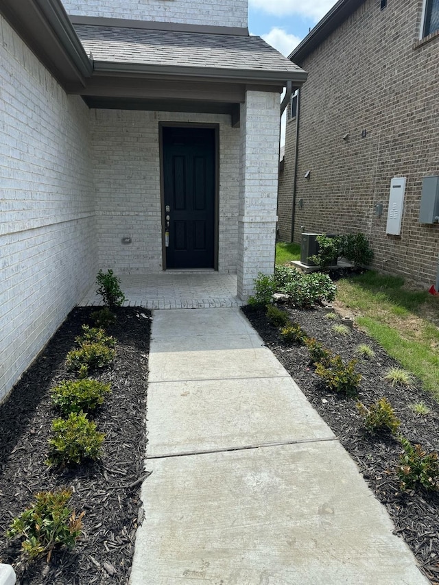 view of exterior entry with brick siding and a shingled roof