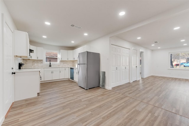 kitchen with visible vents, a sink, freestanding refrigerator, light wood-style floors, and dishwashing machine