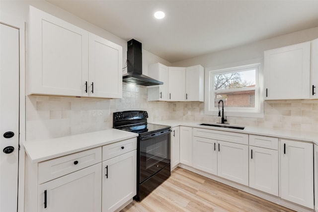 kitchen featuring electric range, light wood-type flooring, a sink, wall chimney exhaust hood, and white cabinets