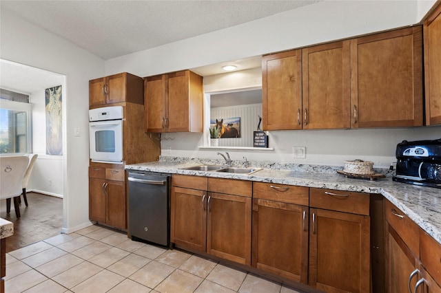 kitchen featuring a sink, light tile patterned floors, brown cabinets, white oven, and stainless steel dishwasher