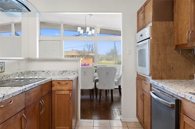 kitchen with white oven, brown cabinets, dishwasher, and a chandelier