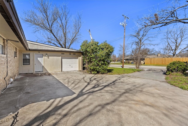 view of property exterior with an attached garage, concrete driveway, and fence