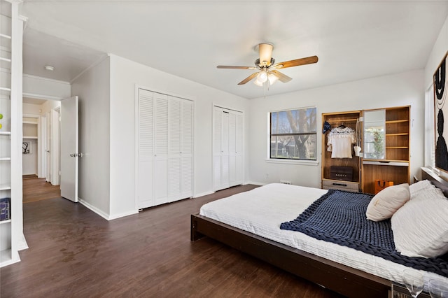 bedroom featuring baseboards, multiple closets, dark wood-type flooring, and a ceiling fan