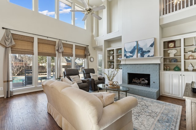 living room featuring dark wood finished floors, a fireplace, a ceiling fan, and built in shelves