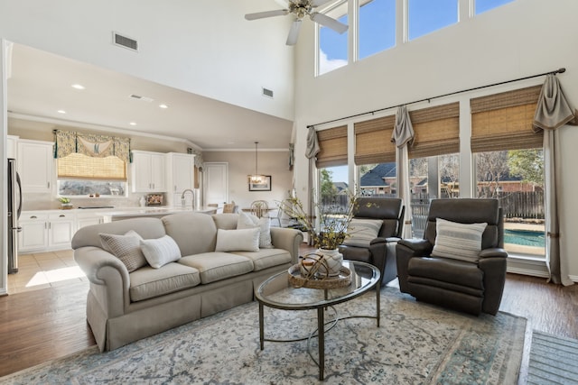 living room with ceiling fan, visible vents, light wood-style floors, and ornamental molding