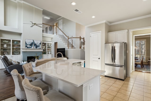 kitchen featuring a breakfast bar area, visible vents, freestanding refrigerator, crown molding, and a brick fireplace