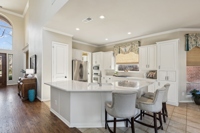 kitchen with a large island, visible vents, appliances with stainless steel finishes, and ornamental molding